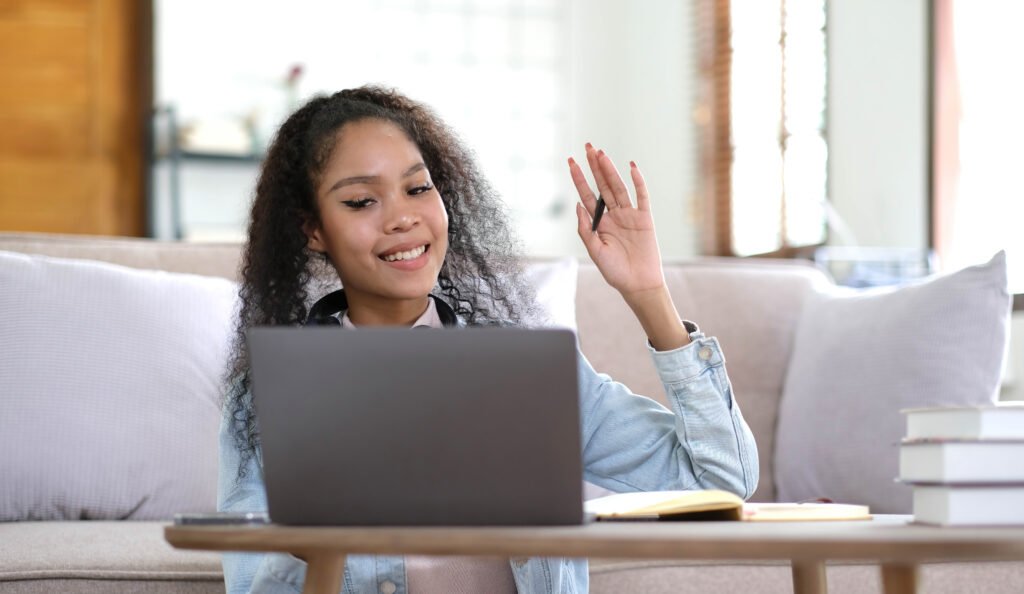 Overjoyed millennial female student in headphones look at laptop screen study online from home. Happy young mixed race woman in earphones talk on video call with teacher. Virtual event concept.